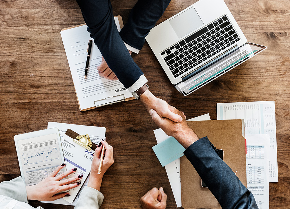 Two people shaking hands over a desk